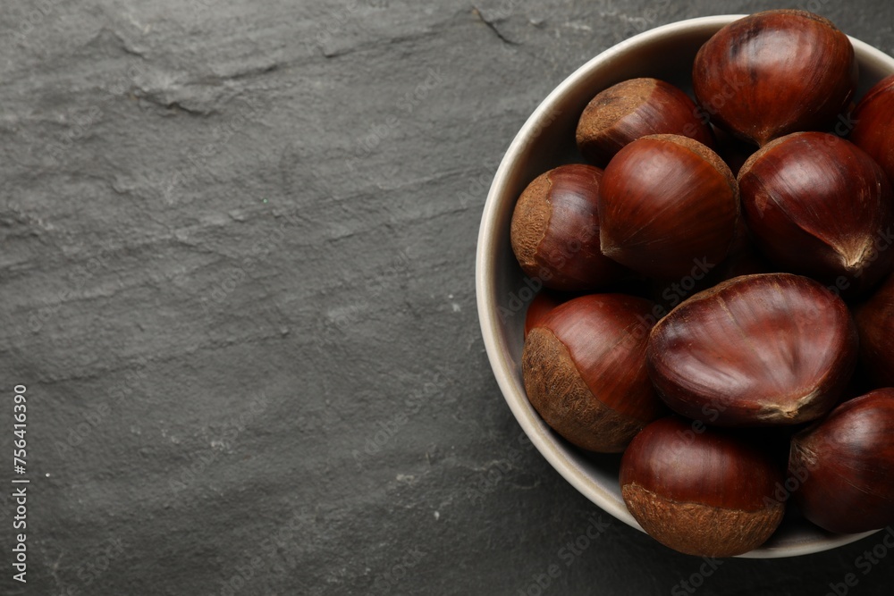 Roasted edible sweet chestnuts in bowl on grey textured table, top view. Space for text Roasted edible sweet chestnuts in bowl on grey textured table, top view. Space for text