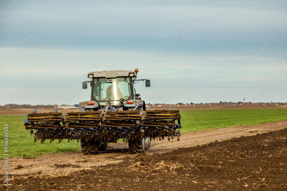 Fototapeta premium Agricultural scene of a tractor plowing dry soil, kicking up dust with a dramatic sky overhead