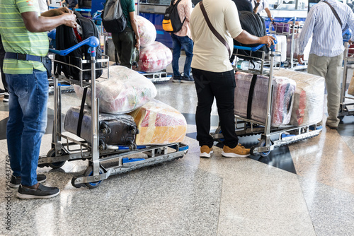 Passenger travelers at airport with luggages on trolley wrapped with protective film for safety