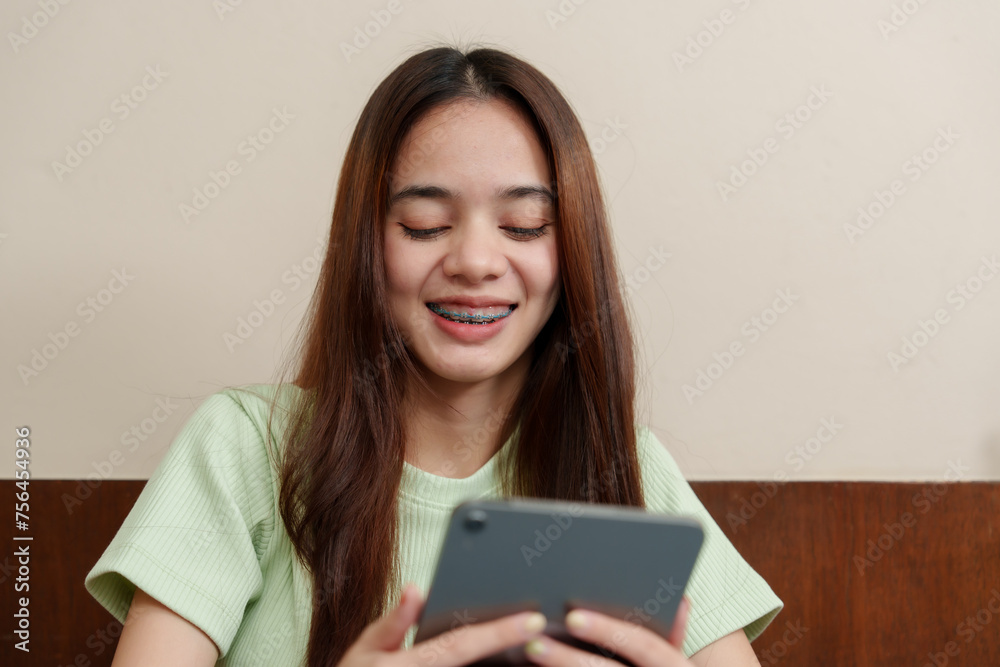 Enthusiastic Asian female student grins while using tablet, seated at work desk in home environment. Cheerful young learner engaged with her digital pad, comfortably working from her home study space Enthusiastic Asian female student grins while using tablet, seated at work desk in home environment. Cheerful young learner engaged with her digital pad, comfortably working from her home study space