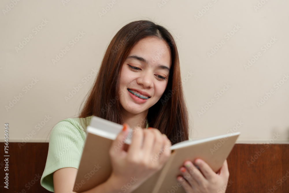 Engrossed Asian female with smile, braces, noting down in book, in serene environment, wearing soft-toned apparel. Absorbed young individual with dental brackets, jotting in notepad, exuding calm Engrossed Asian female with smile, braces, noting down in book, in serene environment, wearing soft-toned apparel. Absorbed young individual with dental brackets, jotting in notepad, exuding calm