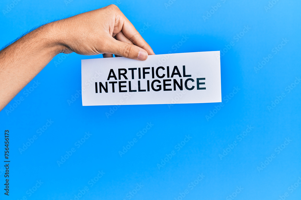Hand of caucasian man holding paper with artificial intelligence message over isolated blue background Hand of caucasian man holding paper with artificial intelligence message over isolated blue background