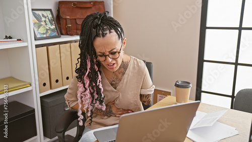 Distressed hispanic woman, an amputee business worker, grappling with stomachache at office while working on laptop