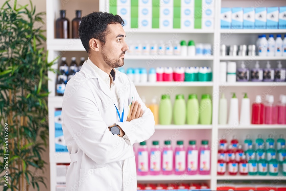 Handsome hispanic man working at pharmacy drugstore looking to the side with arms crossed convinced and confident