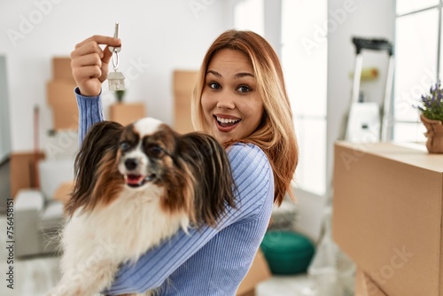 Young caucasian woman smiling confident holding key and dog at new home