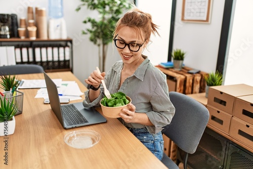Young caucasian woman business worker using laptop eating salad at office