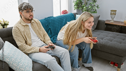 A man and woman sitting together on a gray sofa in a living room, engaged in playing a video game photo