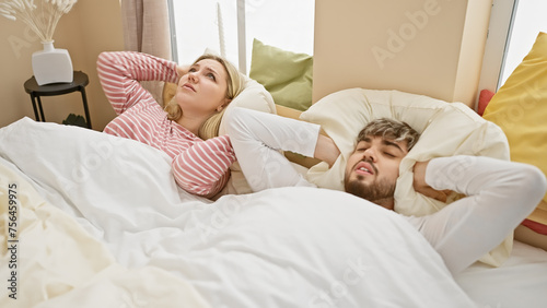 Obraz na płótnie Couple annoyed by loud noise in a bright bedroom, depicting a frustrated woman and a man covering ears