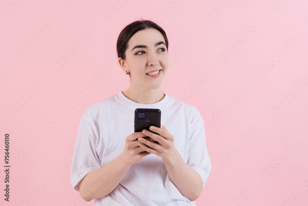 Attractive Caucasian young brunette woman in casual clothes smiling and using mobile phone isolated on pink studio background. Technology, wireless, freelance, work. Attractive Caucasian young brunette woman in casual clothes smiling and using mobile phone isolated on pink studio background. Technology, wireless, freelance, work.