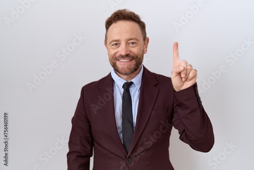 Middle age business man with beard wearing suit and tie showing and pointing up with finger number one while smiling confident and happy.
