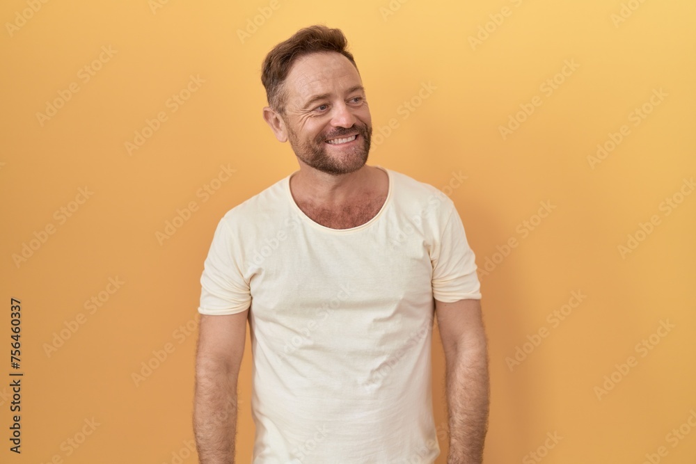 Middle age man with beard standing over yellow background looking away to side with smile on face, natural expression. laughing confident. Middle age man with beard standing over yellow background looking away to side with smile on face, natural expression. laughing confident.