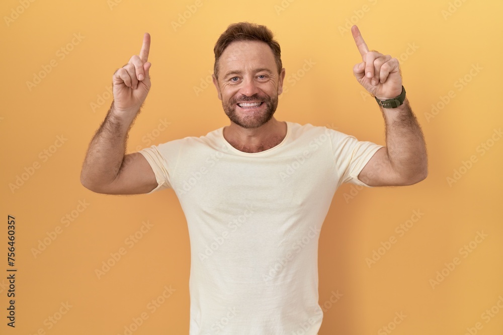 Middle age man with beard standing over yellow background smiling amazed and surprised and pointing up with fingers and raised arms. Middle age man with beard standing over yellow background smiling amazed and surprised and pointing up with fingers and raised arms.