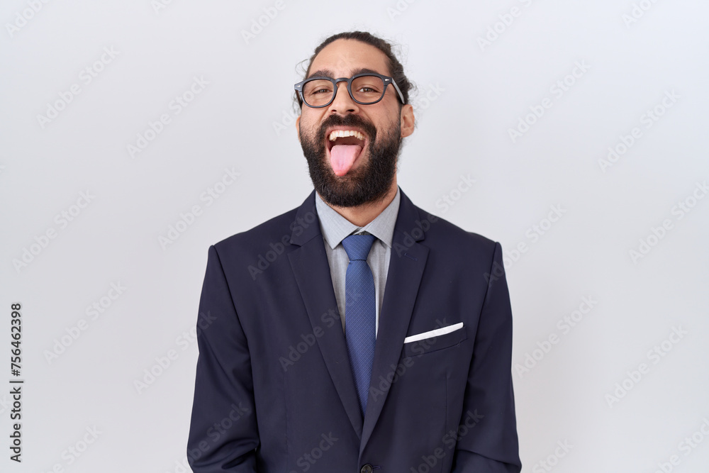Hispanic man with beard wearing suit and tie sticking tongue out happy with funny expression. emotion concept. Hispanic man with beard wearing suit and tie sticking tongue out happy with funny expression. emotion concept.