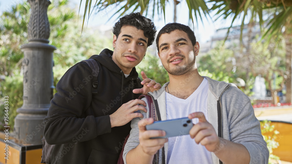 Two hispanic men sharing a moment taking a selfie together on a sunny park day.