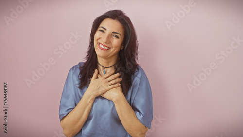 Happy mature hispanic woman in blue clothing isolated on a pink background expressing joy and positivity.