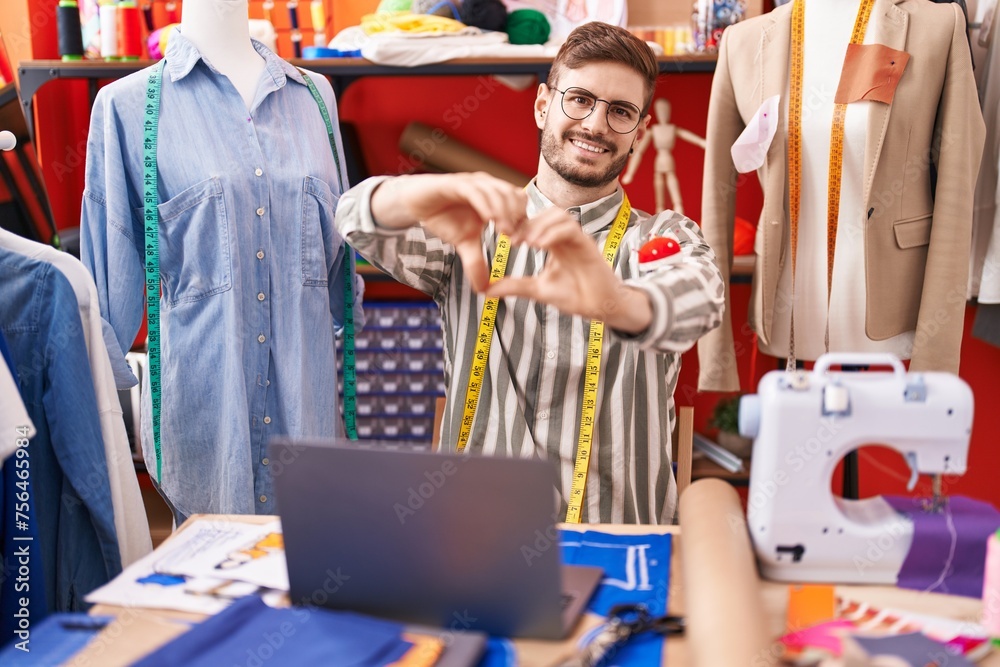 Hispanic man with beard using laptop at tailor room smiling in love showing heart symbol and shape with hands. romantic concept. Hispanic man with beard using laptop at tailor room smiling in love showing heart symbol and shape with hands. romantic concept.