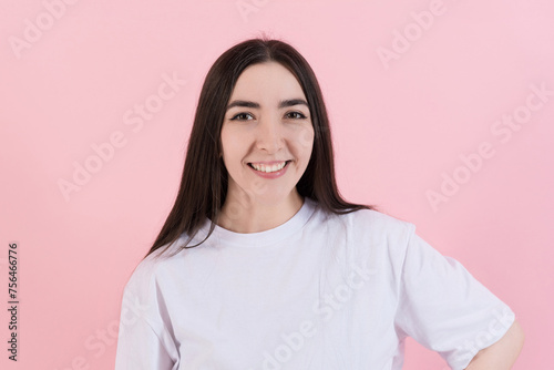 Portrait of attractive Caucasian young brunette woman in casual clothes white t-shirt, smiling and looking confidently at the camera isolated on pink studio background.