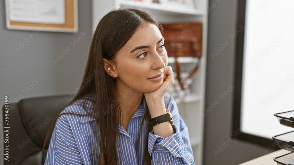 A contemplative young hispanic woman in a striped shirt poses in a modern office setting, exuding professionalism and calm. A contemplative young hispanic woman in a striped shirt poses in a modern office setting, exuding professionalism and calm.