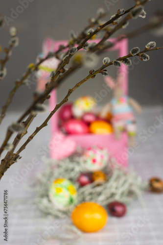 Holiday laid table for Easter celebration with colorful hand-painted Easter eggs in pink wooden basket, toy bunnies, willow branches and Easter cakes