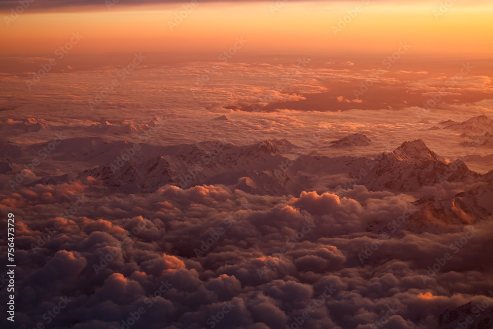Sunset over Italian Alps. Aerial photo with the amazing mountain peaks covered with snow from Alps Mountains and sea of clouds between them. Nature landscape with mountains in sunset light.