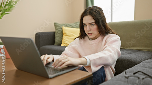 A focused caucasian woman using a laptop in a modern living room setup, evincing productivity and comfort. © Krakenimages.com