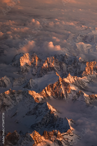 Sunset over Italian Alps. Aerial vertical photo with the amazing mountain peaks covered with snow from Alps Mountains and sea of clouds between them. Nature landscape with mountains in sunset light.