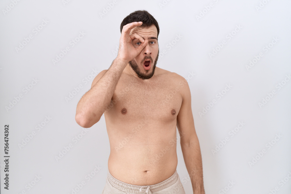 Fototapeta premium Young hispanic man standing shirtless over white background doing ok gesture shocked with surprised face, eye looking through fingers. unbelieving expression.