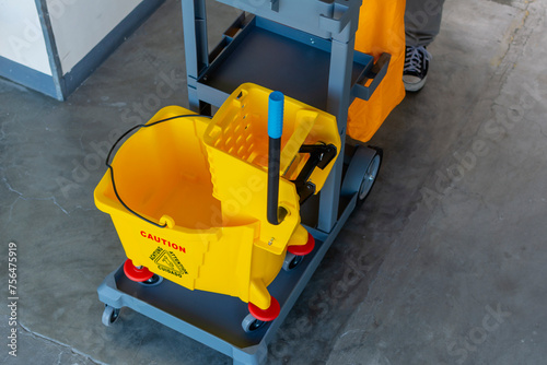 Fotografie A well-equipped janitorial cart complete with a yellow mop bucket and caution sign, ready for office cleaning tasks