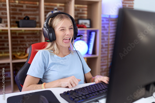 Young caucasian woman playing video games wearing headphones sticking tongue out happy with funny expression. emotion concept.