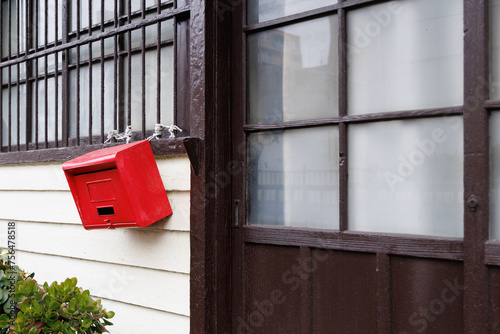 古い木造の建物の入口の前に設置された赤い郵便受け photo