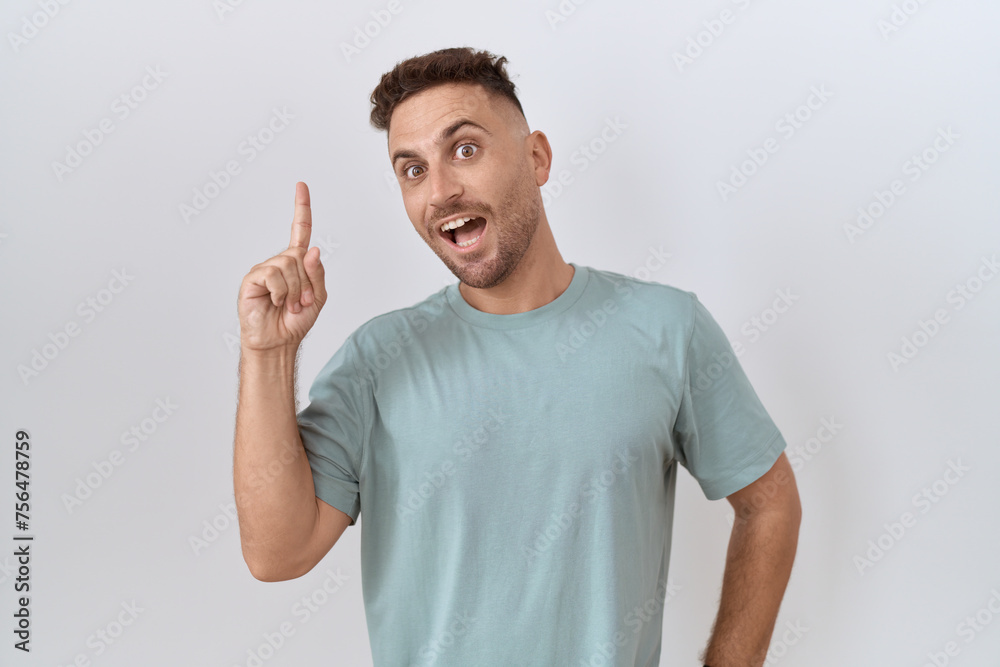 Hispanic man with beard standing over white background pointing finger up with successful idea. exited and happy. number one.
