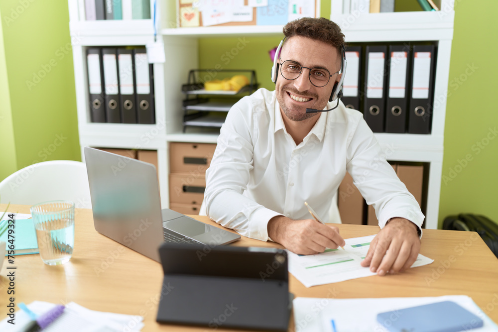 Young hispanic man call center agent writing on document working at office Young hispanic man call center agent writing on document working at office