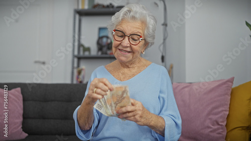 A cheerful senior woman counts czech koruna currency indoors, sitting in her cozy living room photo