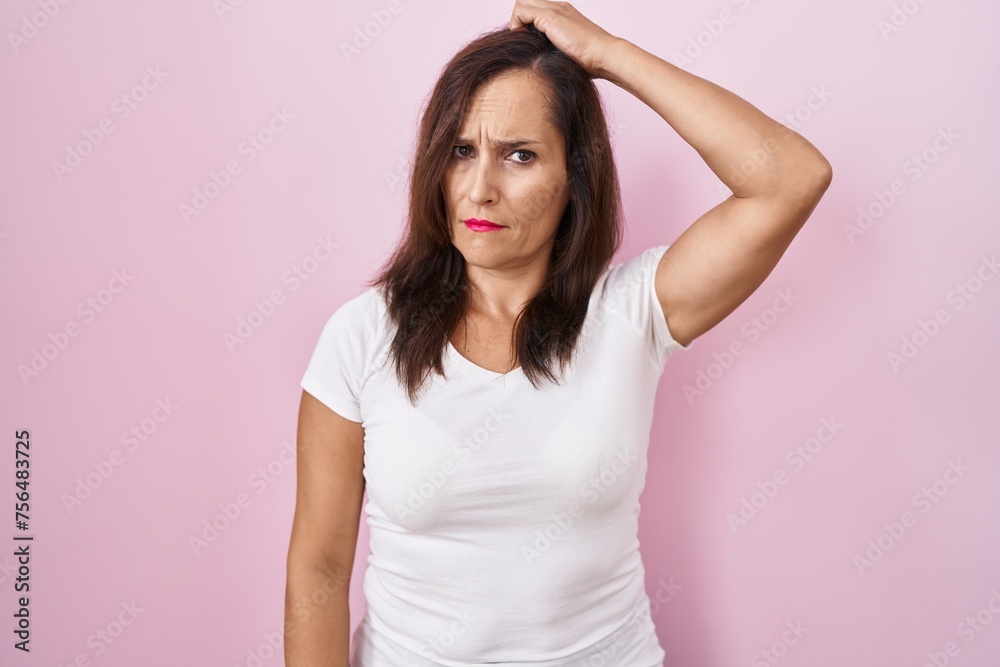 Middle age brunette woman standing over pink background confuse and wondering about question. uncertain with doubt, thinking with hand on head. pensive concept. Middle age brunette woman standing over pink background confuse and wondering about question. uncertain with doubt, thinking with hand on head. pensive concept.
