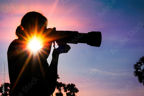 Silhouette of a woman photographer in a palm tree garden at sunrise