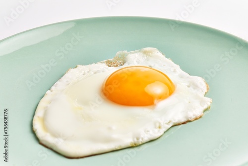 Close-up of a freshly fried egg with a runny yolk on a pale green plate isolated against a white background.