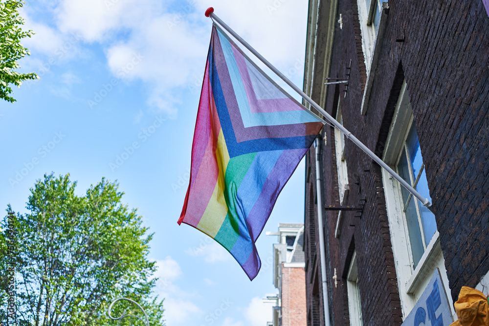 A colorful pride flag waves outside a building against a clear sky, symbolizing lgbtq support and diversity.