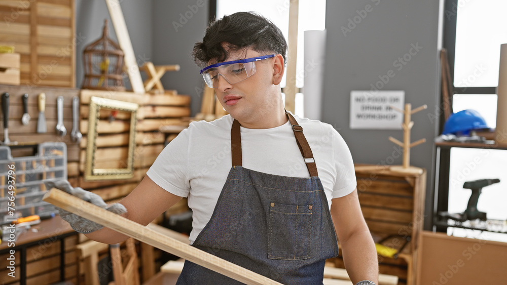 Young man examines wooden plank in a well-equipped carpentry workshop.