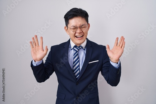 Young asian man wearing business suit and tie celebrating mad and crazy for success with arms raised and closed eyes screaming excited. winner concept