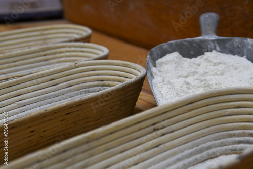 Schaufel mit Mehl neben gestapelten Bastkörben in einer Bäckerei