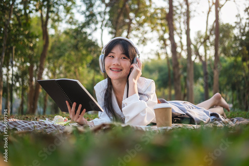 Pretty young woman listening to music in headphone and reading book in the park.