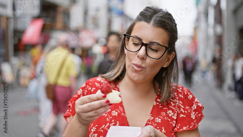 Gorgeous hispanic girl in specs relishing strawberry japanese mochi on osaka's famous dotonbori street photo
