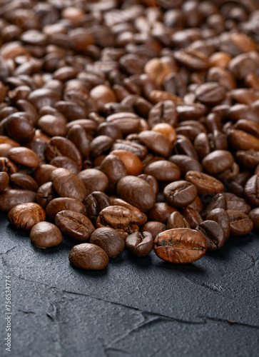Scattered roasted coffee beans by a large pan on a dark background