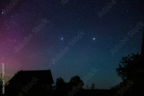 Starry sky with bright stars outside the city in the mountains, no one, the Milky Way. Silhouettes of houses and trees. Starry, night landscape.
