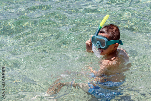 Boy with snorkel and mask in crystal clear sea water, enjoying beach family vacation. Snorkeling, swimming, water sports concept. Summer holidays background, copy space