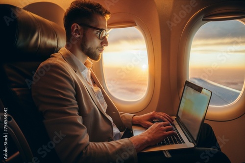 Businessman working on laptop in airplane at sunset. Man in business attire concentrates on his laptop during a flight with a beautiful sunset outside © Mrs__DoubleF
