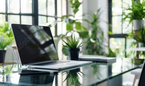 A computer is on a glass desk in an office surrounded by potted plants, creating a peaceful work environment with a touch of nature