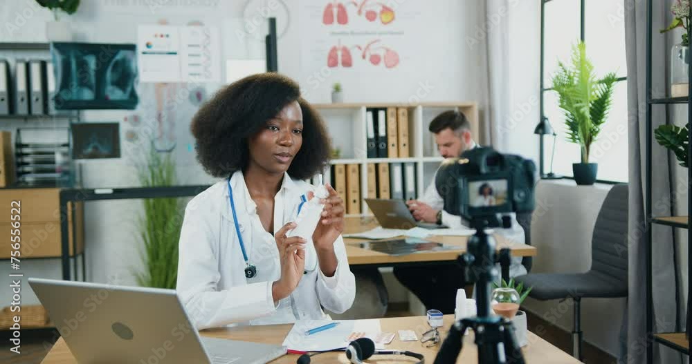 African american woman doctor recording video on camera from modern clinic office and telling about antibacterial spray to internet audience