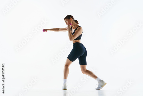 Young woman with slim sportive body training, doing jab exercises with dumbbells isolated over white studio background. Concept of sport, health and body care, fitness app, exercises templates