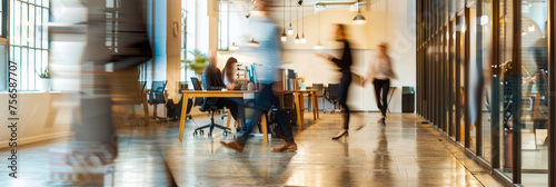 This photo captures a modern office space with several blurred figures of business professionals going about their work. The image conveys a sense of movement and activity within the workplace photo